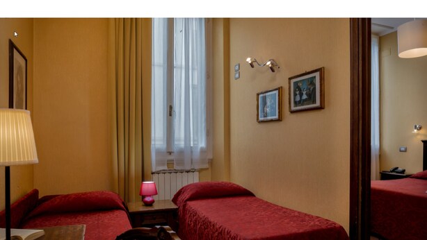 A hotel room with two single beds, a window with curtains, a bedside table with a lamp, and two framed pictures on the wall. - Kursaal & Ausonia (Florence)