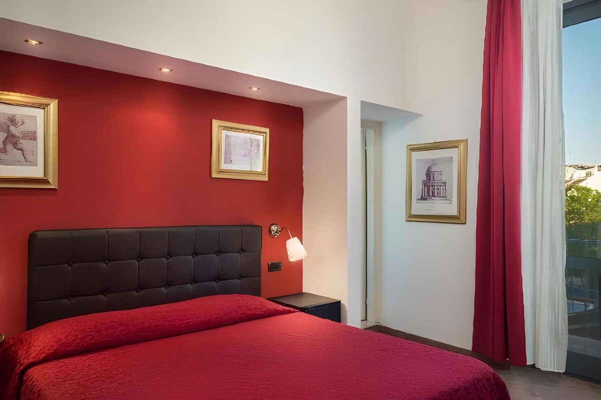 A bedroom with a red wall, a black headboard, a red bedspread, and two framed pictures.