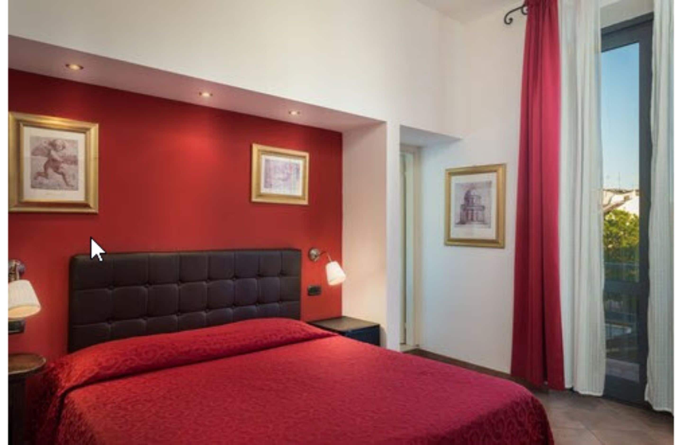 A bedroom with a red wall, a black headboard, and two framed pictures.