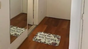A hallway with a wooden floor, a white door, and a large mirror reflecting the door and a light fixture. - Cerviño y Bulnes 2 (Buenos Aires)