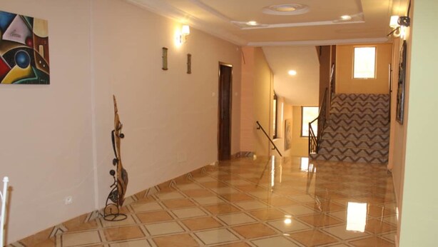 A hallway with a tiled floor, a staircase with a zigzag patterned wall, and a door at the end. - Maison D Hote Villy (Ouagadougou)