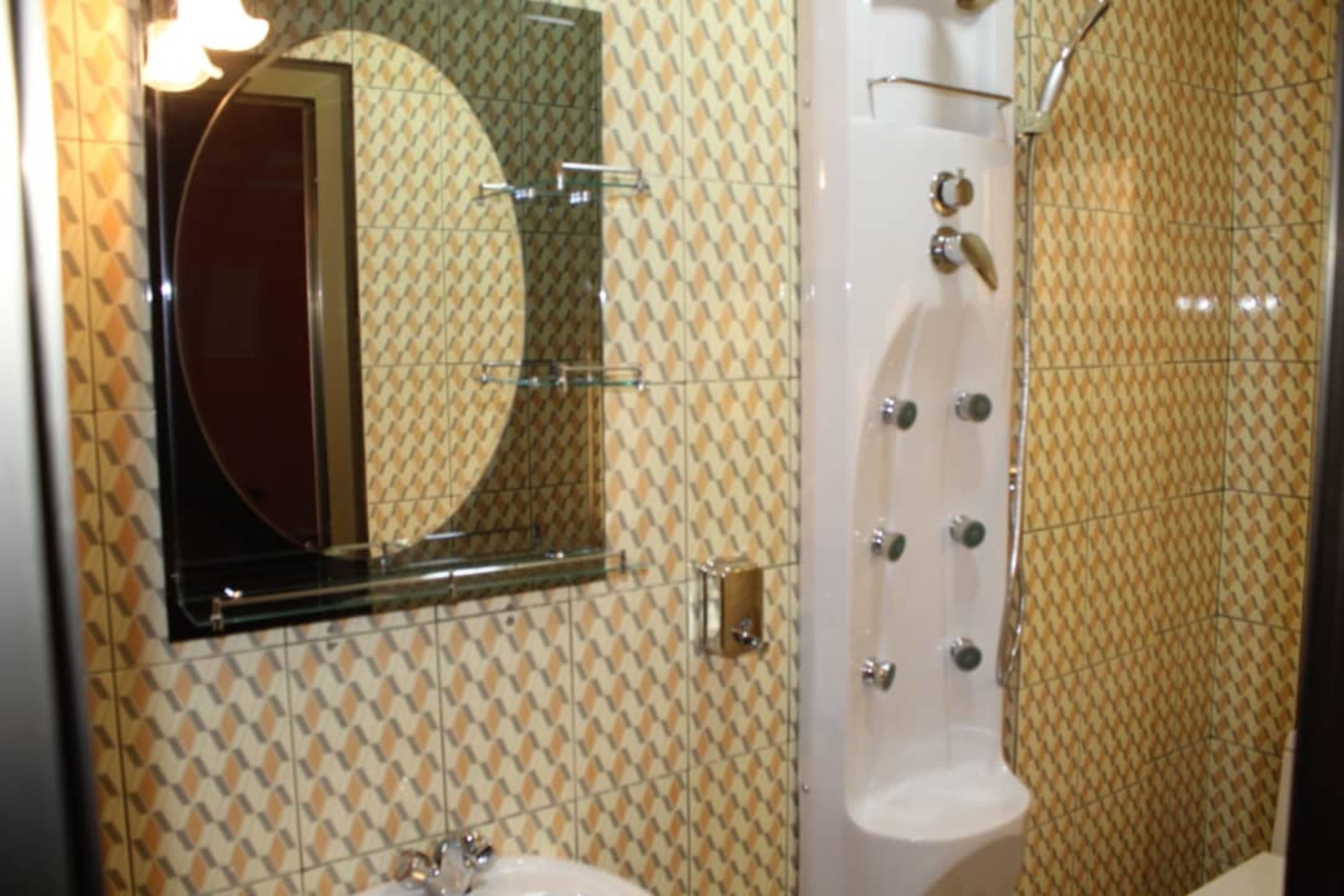 Un baño con azulejos estampados, un espejo redondo, un lavabo y una zona de ducha.