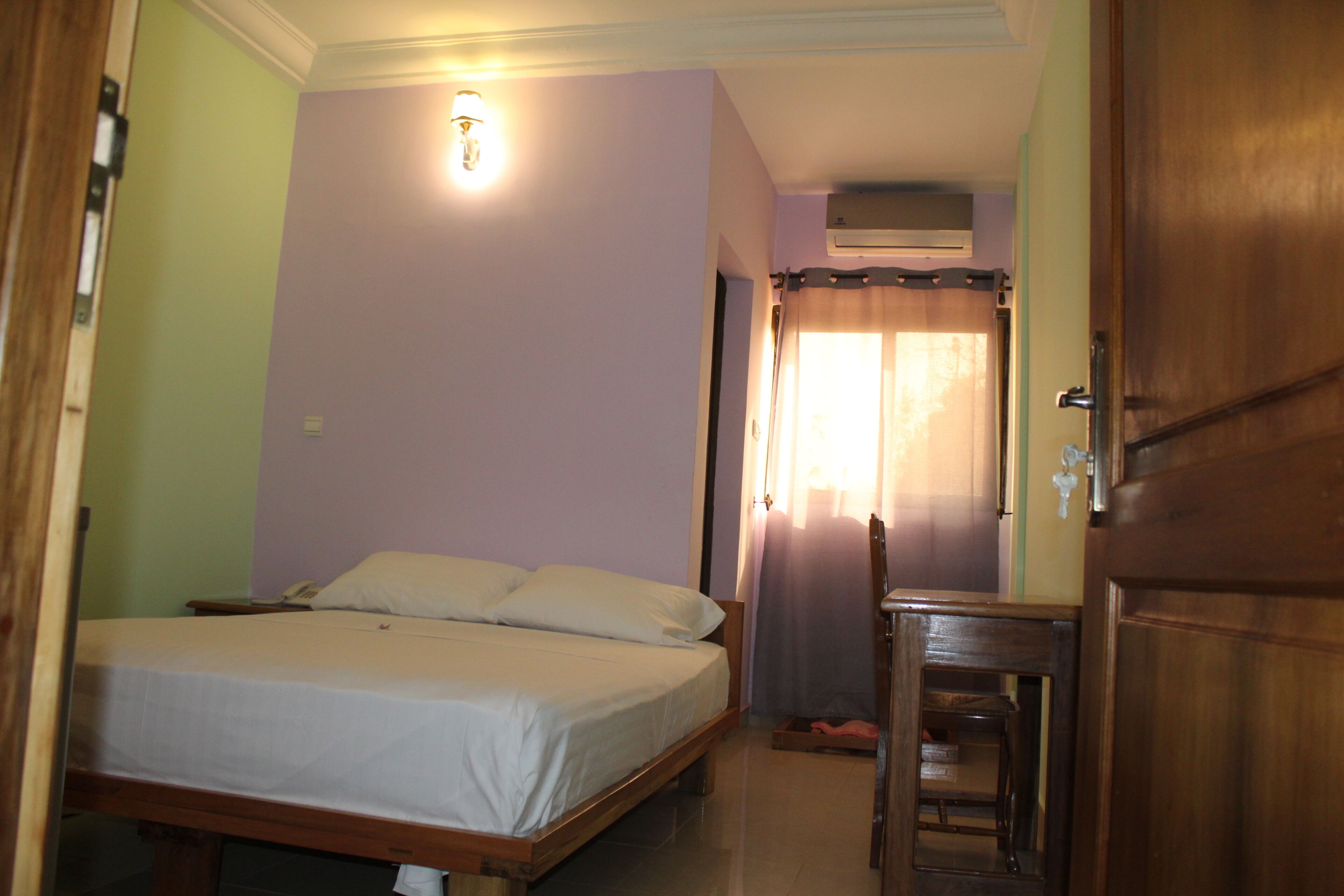 A bedroom with a single bed, a wooden nightstand, a chair, and a door.