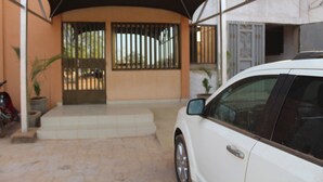 A white car parked under a covered area with a tiled entrance and a metal gate. - Maison D Hote Villy (Ouagadougou)