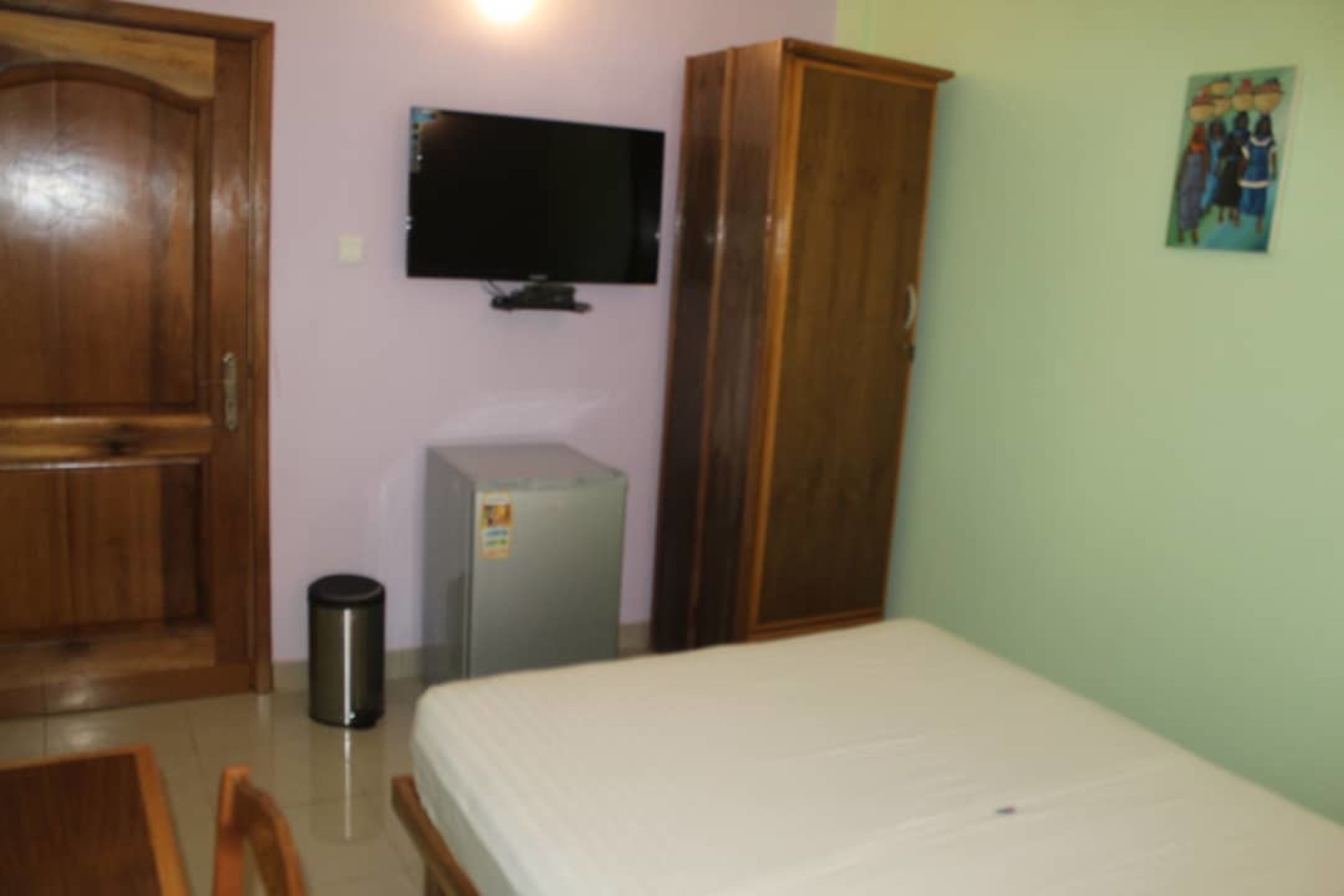 Un dormitorio con cama, televisor montado en la pared, armario y un refrigerador pequeño.