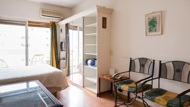 A hotel room with a bed, a small table with a telephone, a chair, a sofa, and a wardrobe. - Cerviño y Bulnes 3 (Buenos Aires)