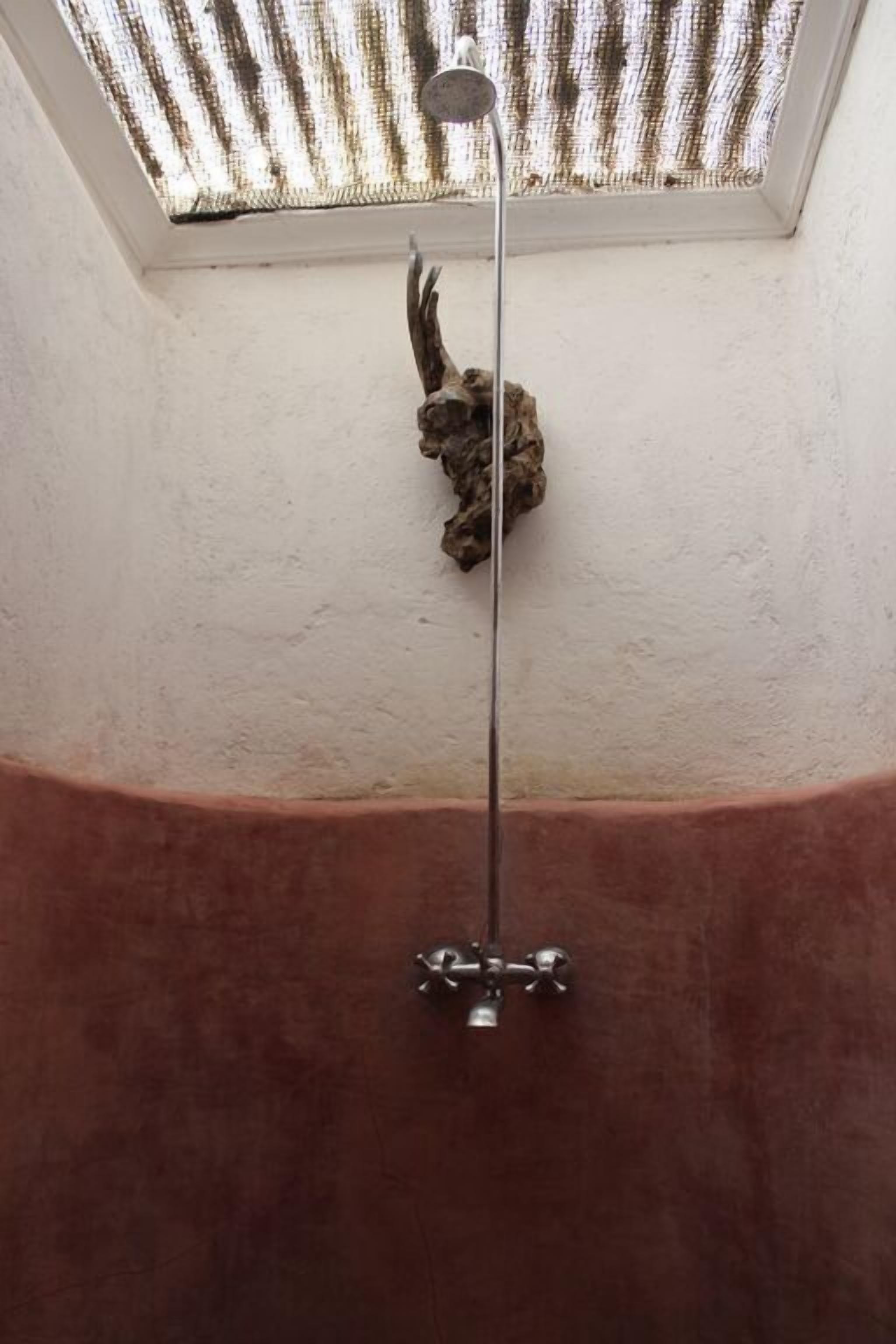 Un tragaluz con cabezal de ducha, una pared de piedra y un suelo rojo.