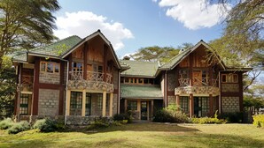 A large, multi-story building with a traditional architectural style, featuring stone and wood construction, multiple balconies, and a well-maintained lawn. - Oleitiko Cottages (Naivasha)