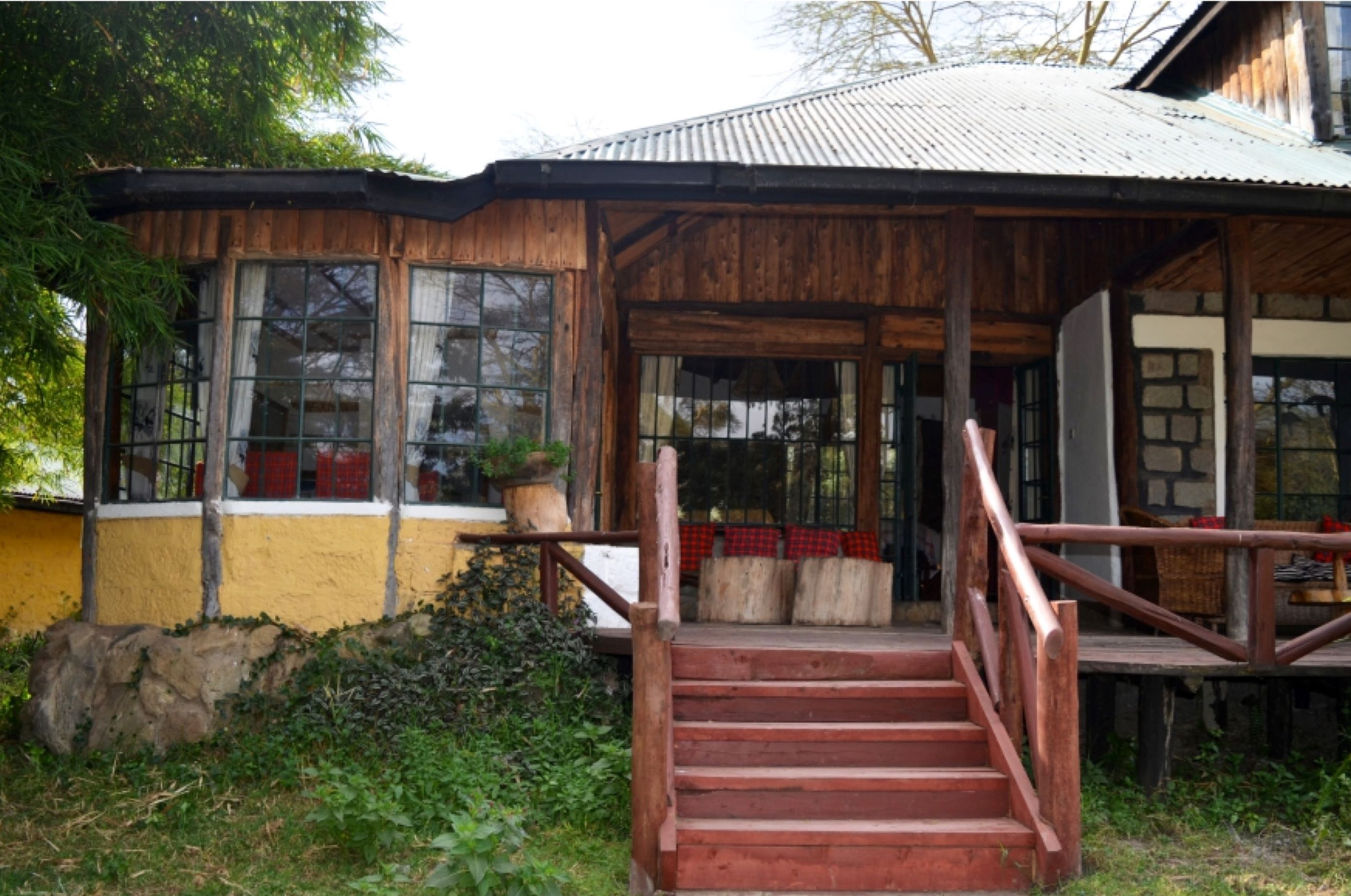 A rustic wooden building with a porch, a staircase leading to the entrance, and a stone wall in the background.