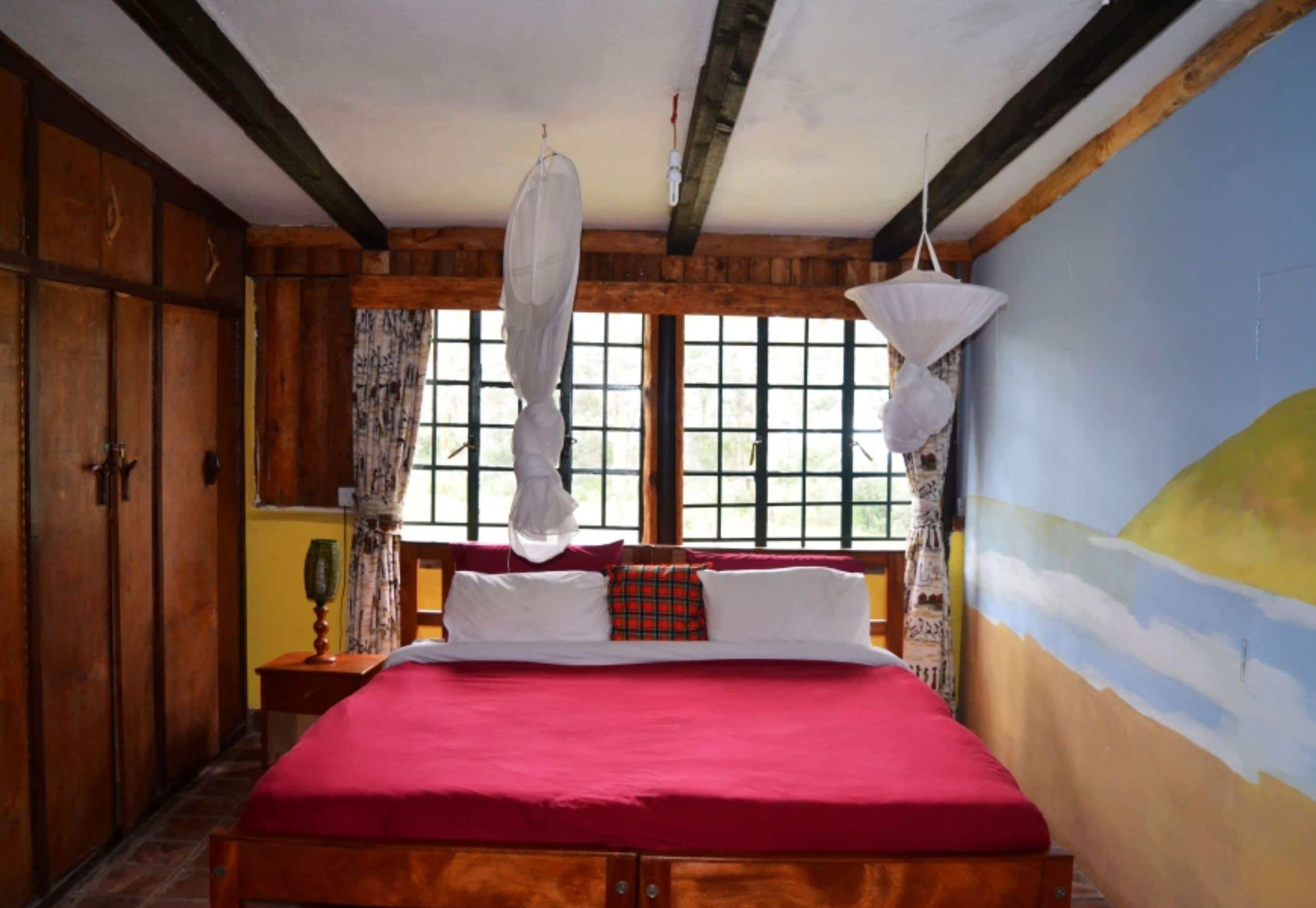 A wooden-framed room with a bed, a window with a view, and a wall with a painting.