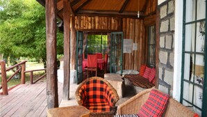 A wooden porch with wicker furniture and a stone wall. - Oleitiko Cottages (Naivasha)