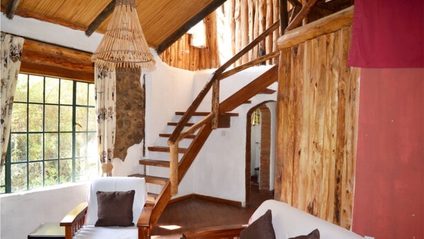 A rustic interior with a wooden staircase, a hanging light fixture, and a view through a window. - Oleitiko Cottages (Naivasha)