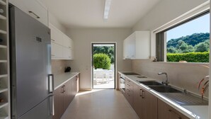 Een moderne keuken met een roestvrijstalen koelkast, witte kastjes, een dubbele spoelbak en uitzicht op groen via een groot raam.