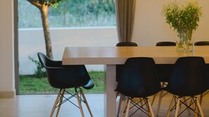 Een moderne eethoek met een grote tafel, zwarte stoelen, een hanglamp en uitzicht op groen.