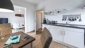 A modern kitchen with white cabinets, a black countertop, and a variety of kitchen utensils hanging on the wall. - Diekhuus Arngast, Apartment Butendiek - Apartment Butendiek in the Diekhuus (Varel)