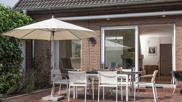 An outdoor patio with a table and chairs, a large umbrella, and a stroller. - Diekhuus Arngast, Apartment Butendiek - Apartment Butendiek in the Diekhuus (Varel)