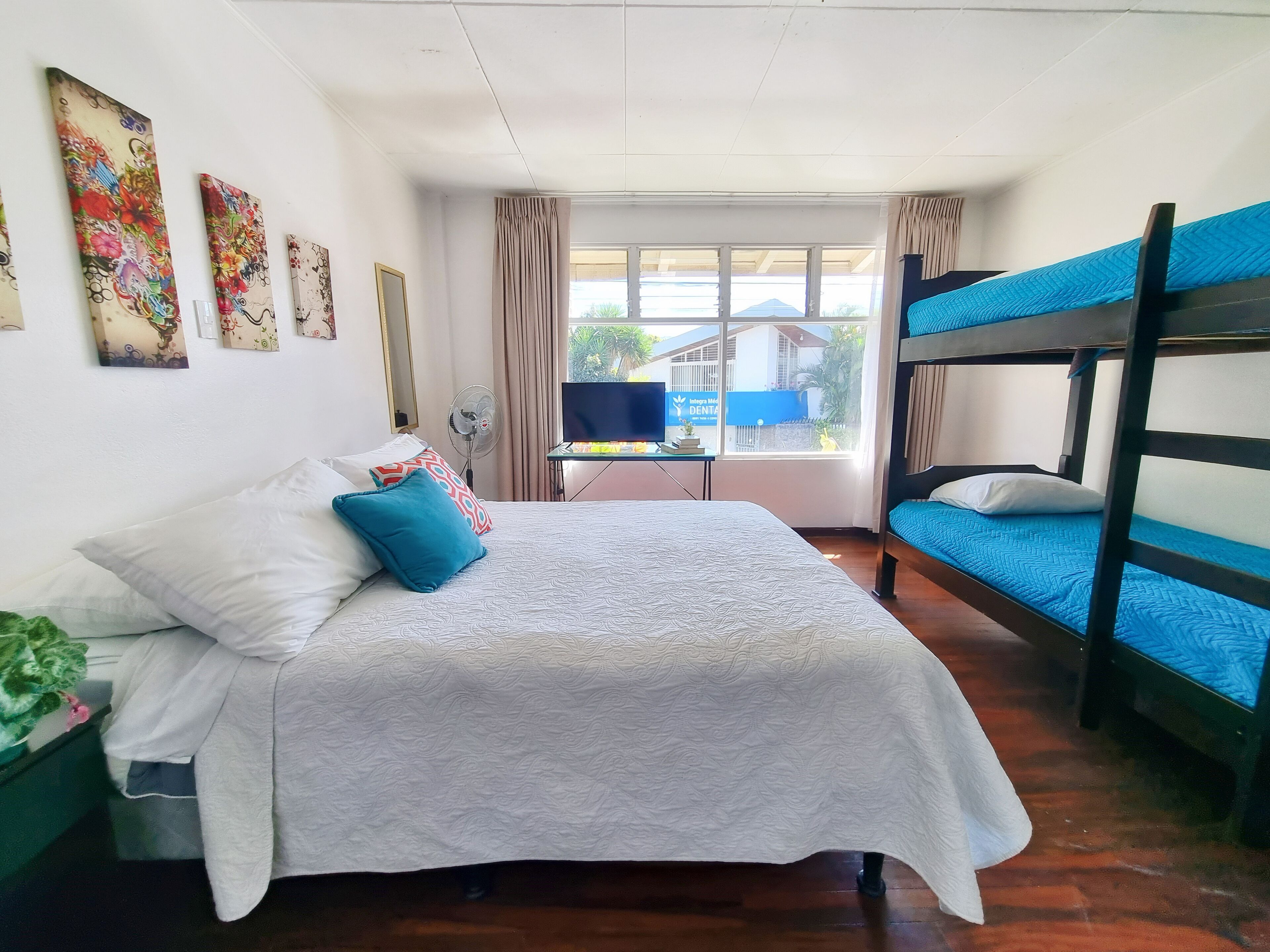 Une chambre d’hôtel avec un lit superposé, un bureau avec un ordinateur, une télévision et une fenêtre donnant sur un immeuble.