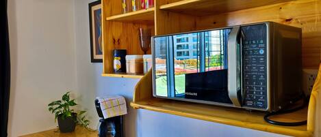 Una cocina con microondas integrado, cafetera y repisas de madera con frascos y una foto enmarcada.