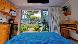 A bedroom with a bed, a television, a fan, and a view of a garden through a sliding door. - Casa Jardin Del Mango (San José)
