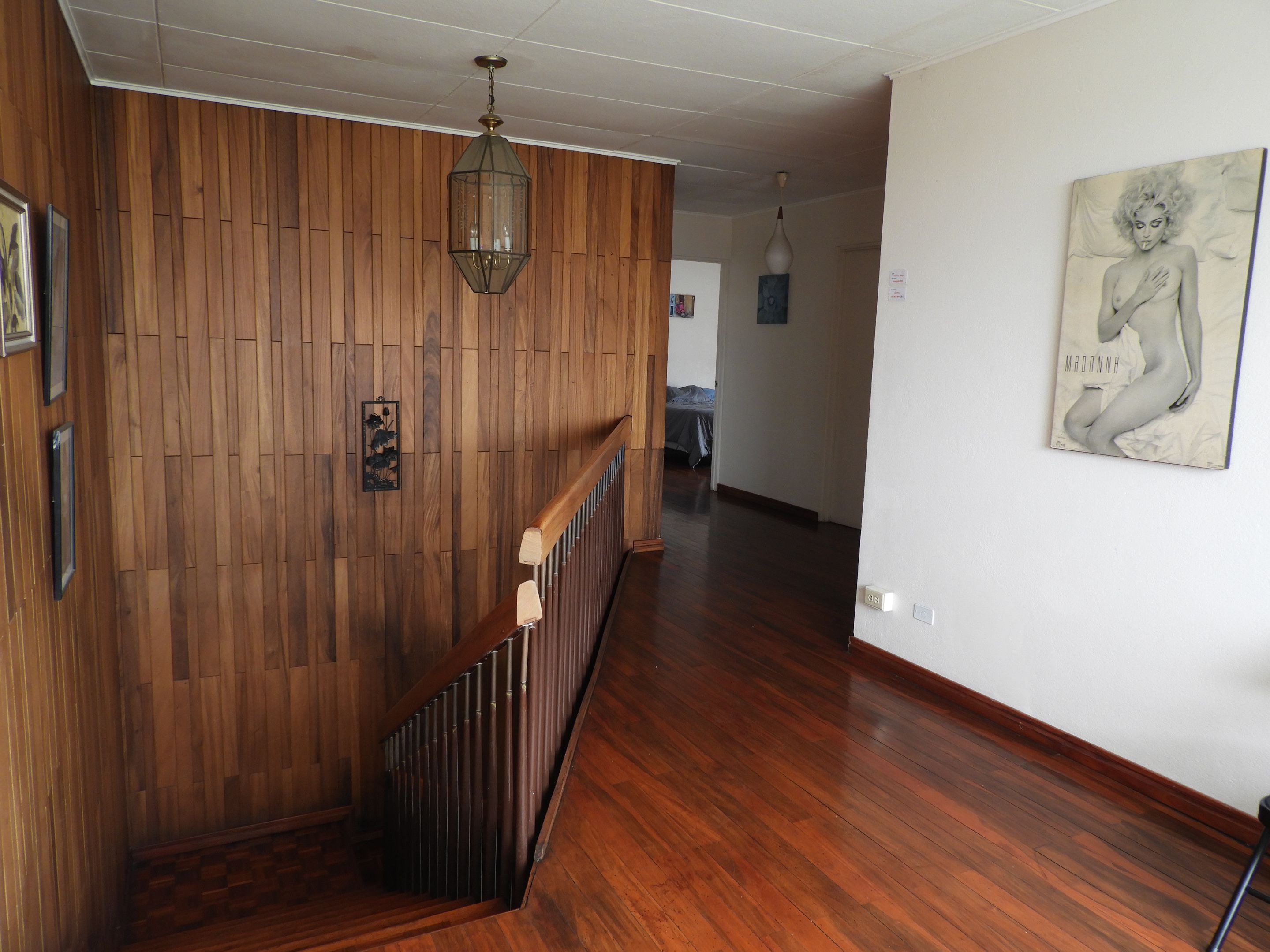 Un interior de fusta amb una escala, una làmpada penjant i una obra d'art penjada a la paret.