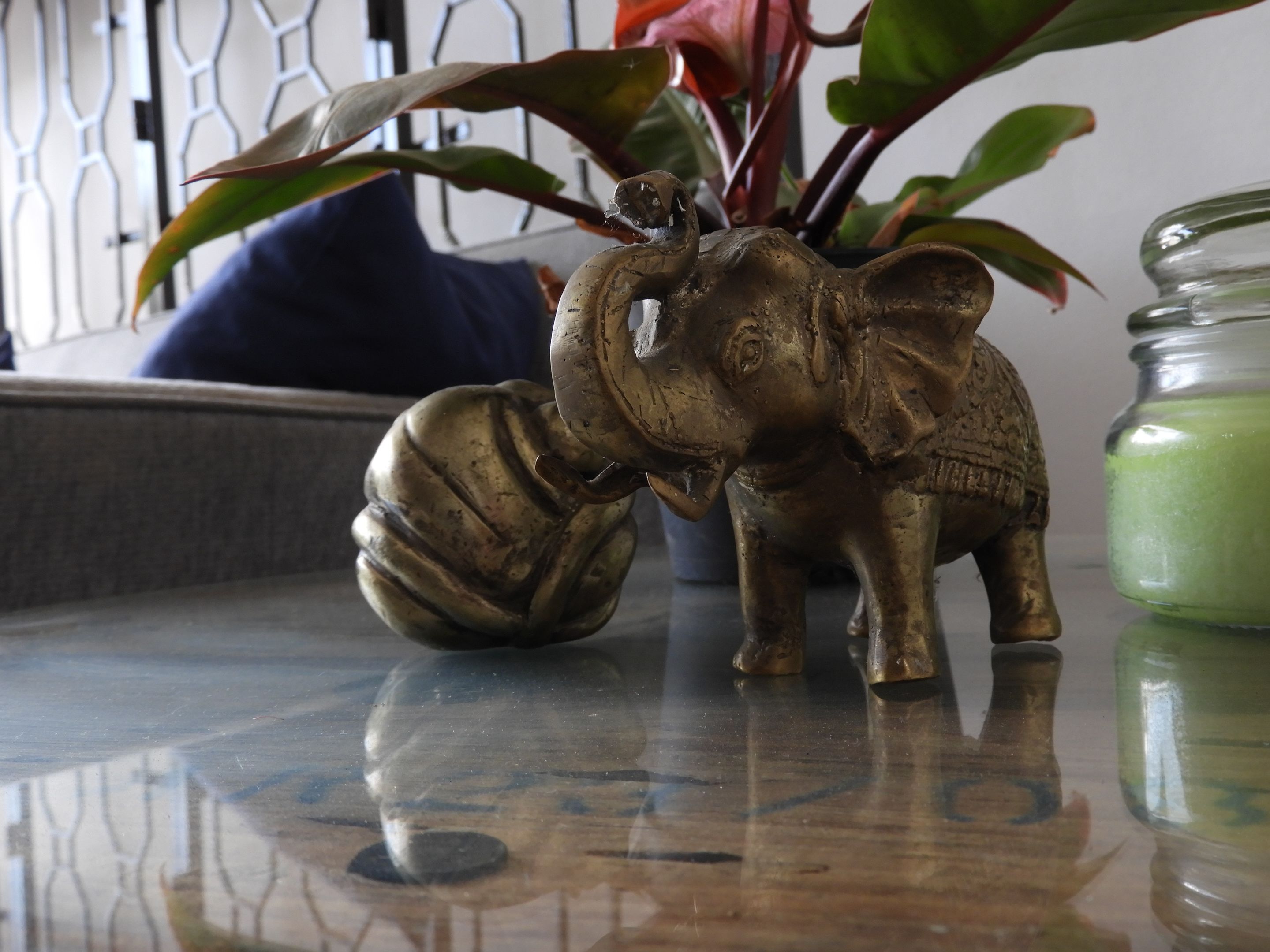 A brass elephant figurine on a reflective surface with a green glass jar nearby.