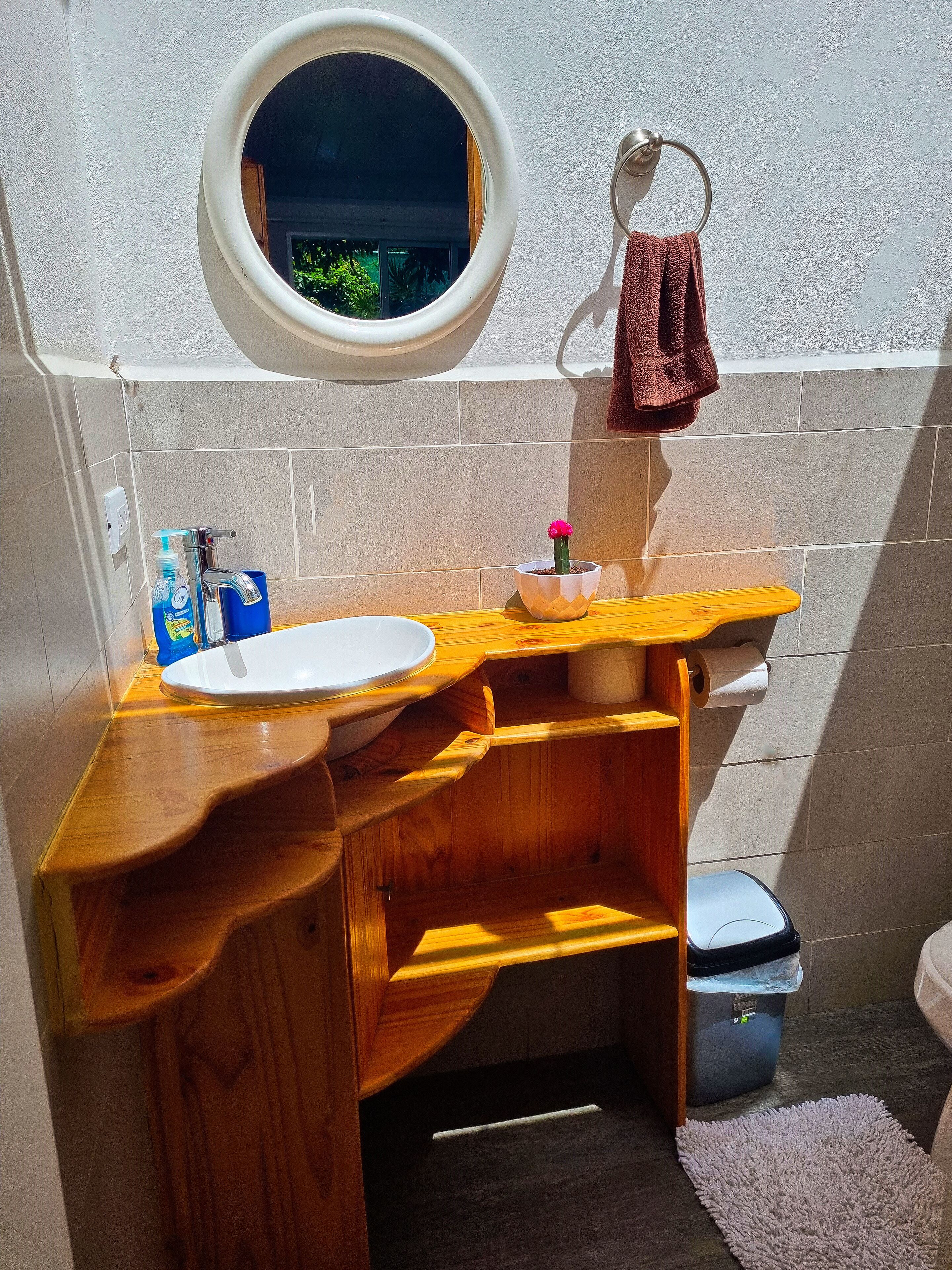 A compact bathroom with a wooden vanity, a round mirror, a towel rack, and a small potted plant.