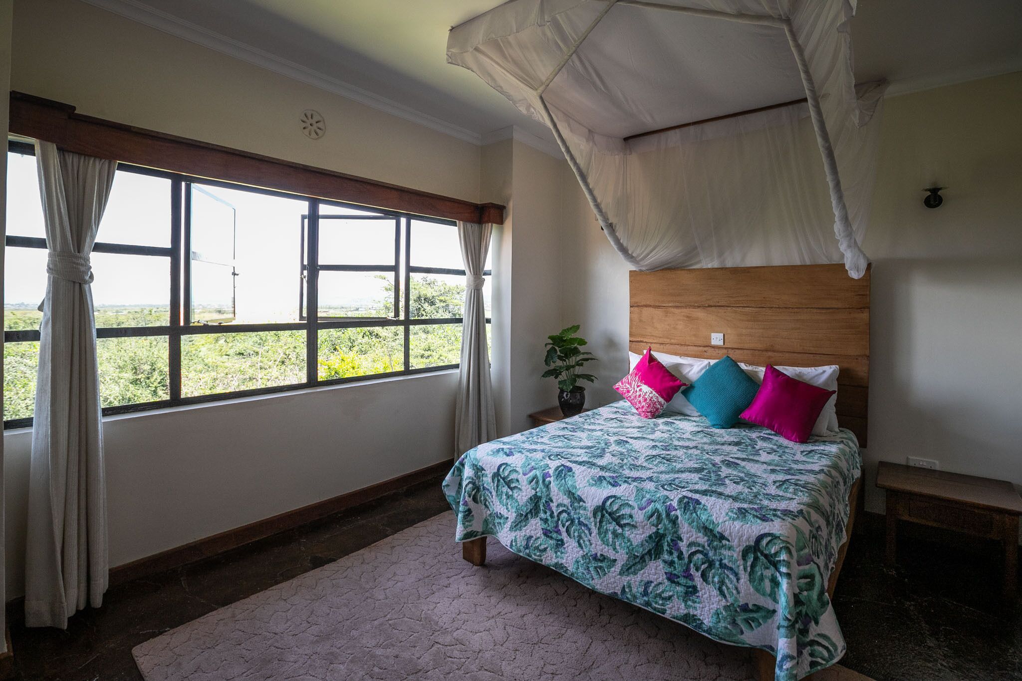 A bedroom with a bed, a window with curtains, a bedside table, and a nightstand.