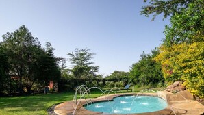 Una piscina circular con borde de piedra, rodeada de césped y varios árboles.