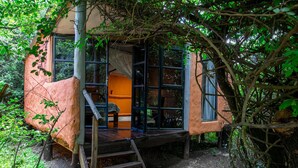 Una casa en el árbol con terraza de madera, una escalera y un ventanal.