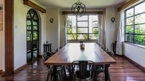 Un comedor amplio con una larga mesa de madera y sillas negras, ventanas grandes con cortinas y una lámpara decorativa en el techo.