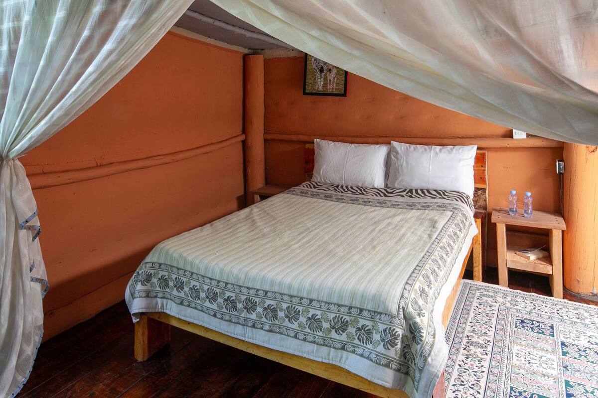 A single bed with a zebra-patterned bedspread, a wooden nightstand with two bottles, and a patterned rug on the floor.