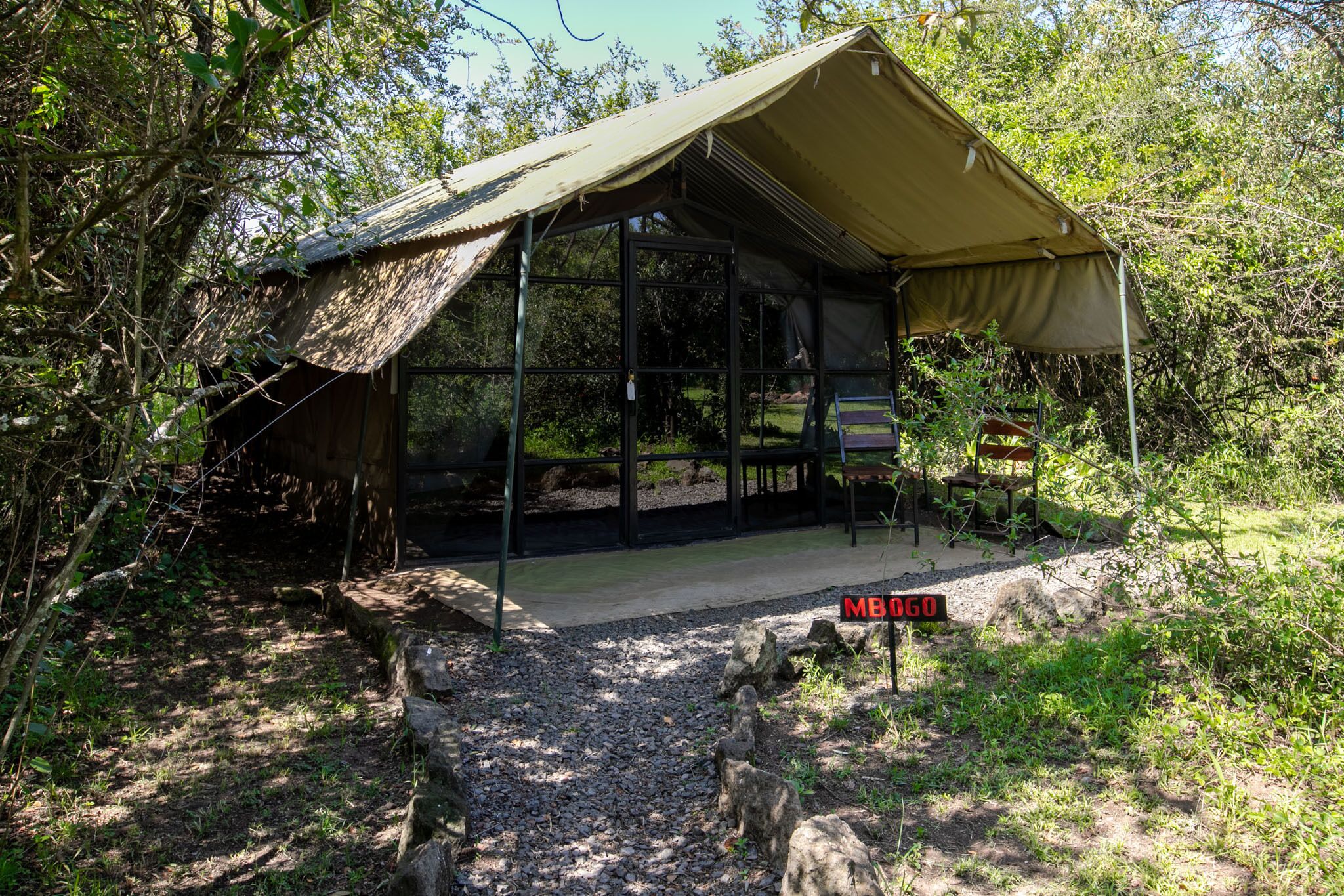 A safari tent with a metal frame and a canvas roof, surrounded by natural vegetation.