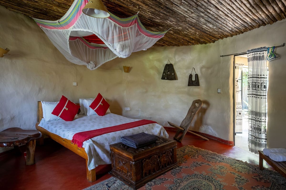 A room with a bed, a wooden chest, a bench, a hanging chair, and a mosquito net.
