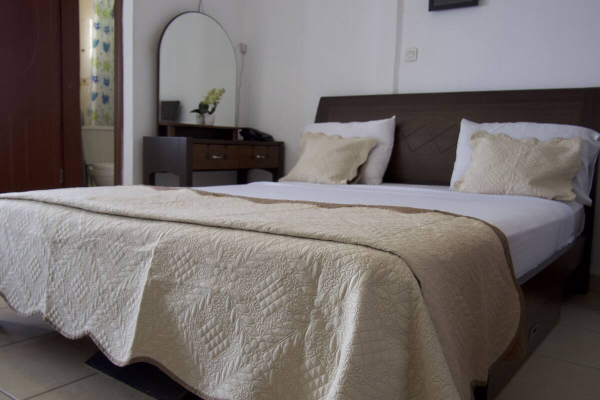 A neatly made bed with a quilted bedspread, a wooden headboard, and two pillows.