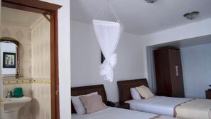 A hotel room with two beds, a bathroom with a sink and mirror, and a wardrobe. - Océanis Hotel (Mutsamudu)
