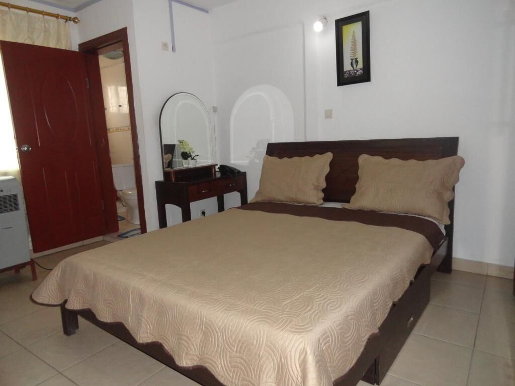 Un dormitorio con una cama, cabecera de madera, cómoda, espejo y una puerta.