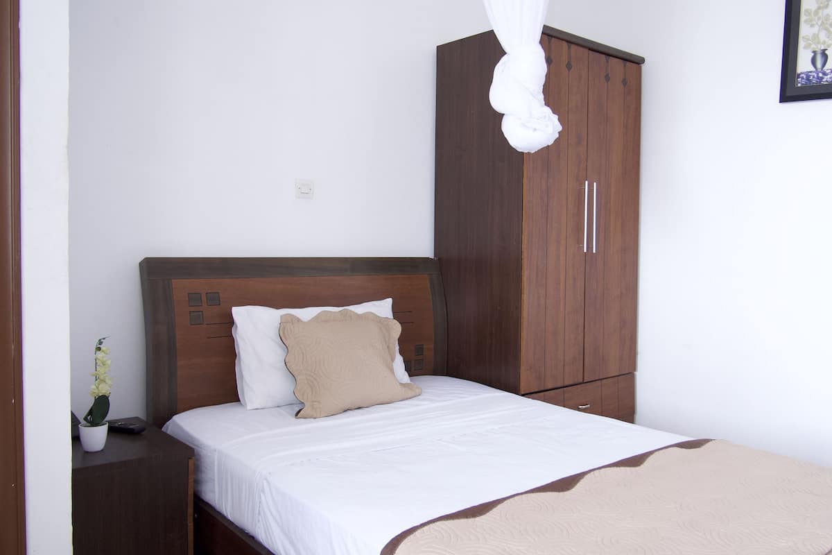 A bedroom with a wooden headboard, a bed with white bedding and a beige throw blanket, a nightstand with a potted plant, and a wardrobe.