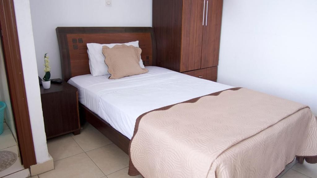 Una cama bien hecha con cabecera de madera, una mesita de noche con una planta y un armario con espejo.