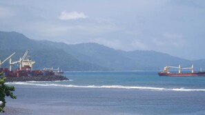 A cargo ship docked at a port with mountains in the background. - Océanis Hotel (Mutsamudu)