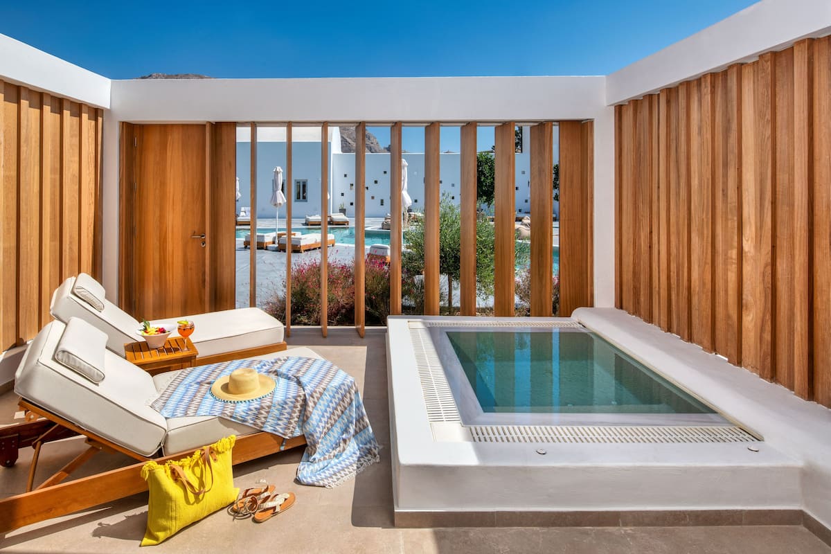 A modern outdoor pool area with a hot tub, lounge chairs, and a view of a pool and mountains.