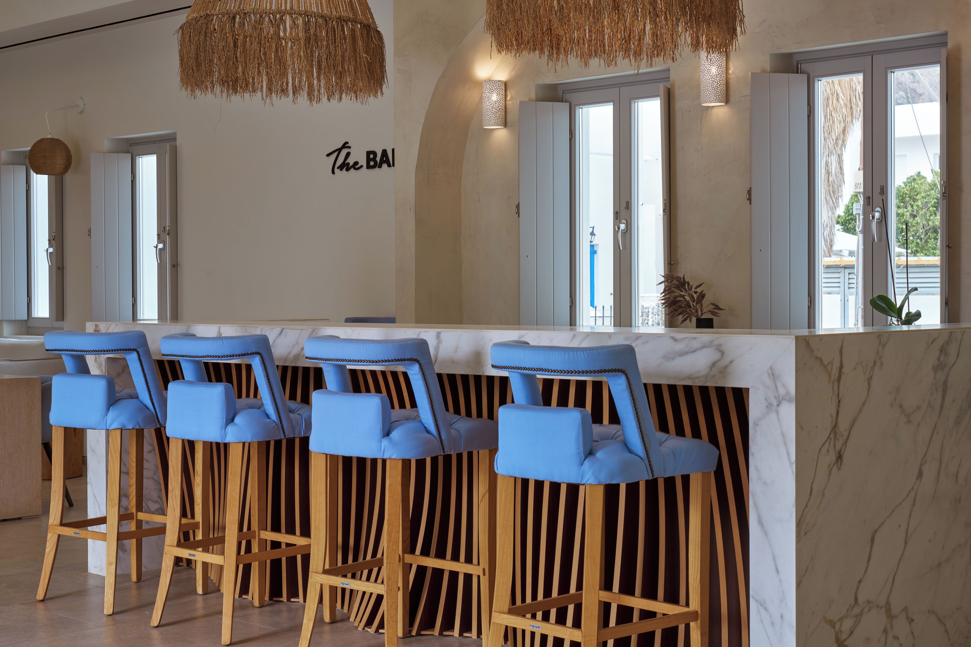 A bar area with four blue bar stools, a marble countertop, and a wall-mounted sign reading "the BA".