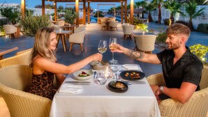 An outdoor dining area with wicker furniture, a pool in the background, and a well-lit ambiance. - Meltemi Blu - Adults Only (Santorini)