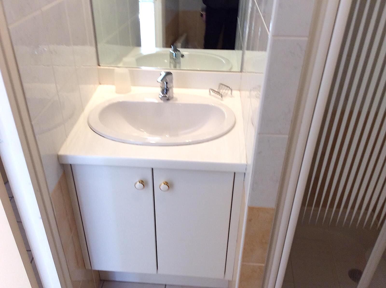 Un baño con un lavamanos blanco, un espejo encima y un mueble blanco debajo.
