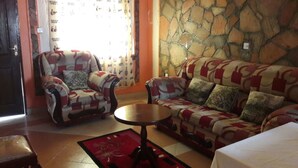 Un salon avec un mur en pierre, un canapé à motifs, un fauteuil et une petite table ronde.