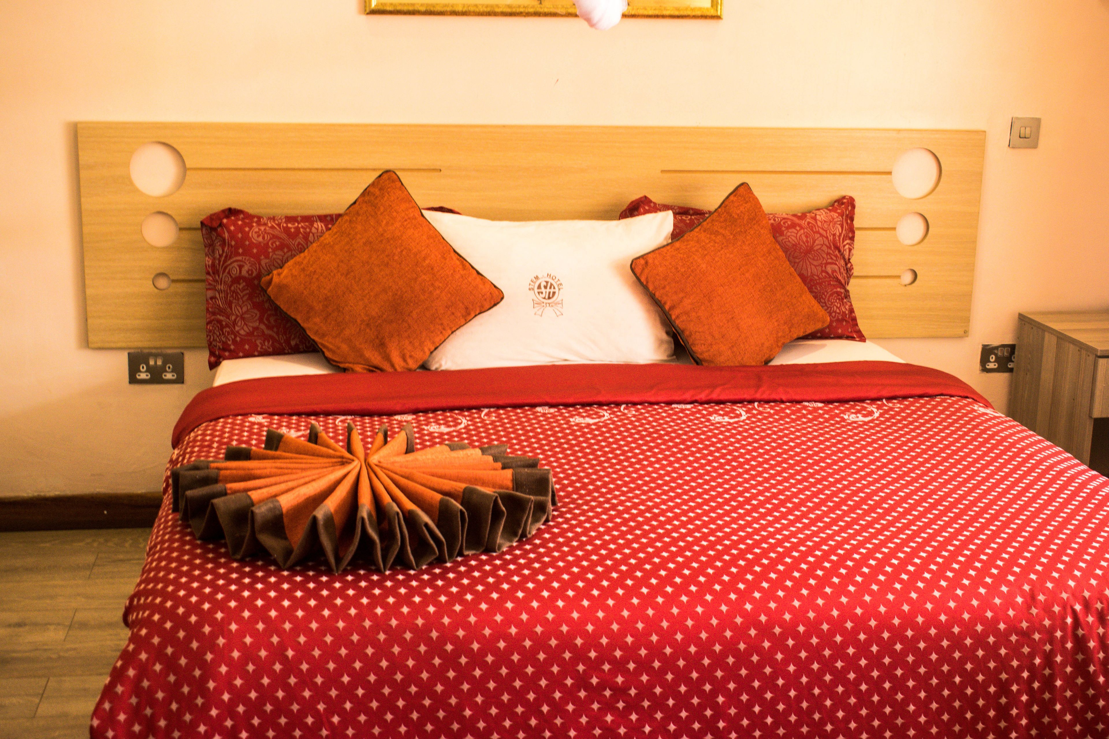 Una cama bien hecha con una colcha de diseño rojo y blanco, dos almohadas rojas y un llamativo cabecero naranja y marrón.
