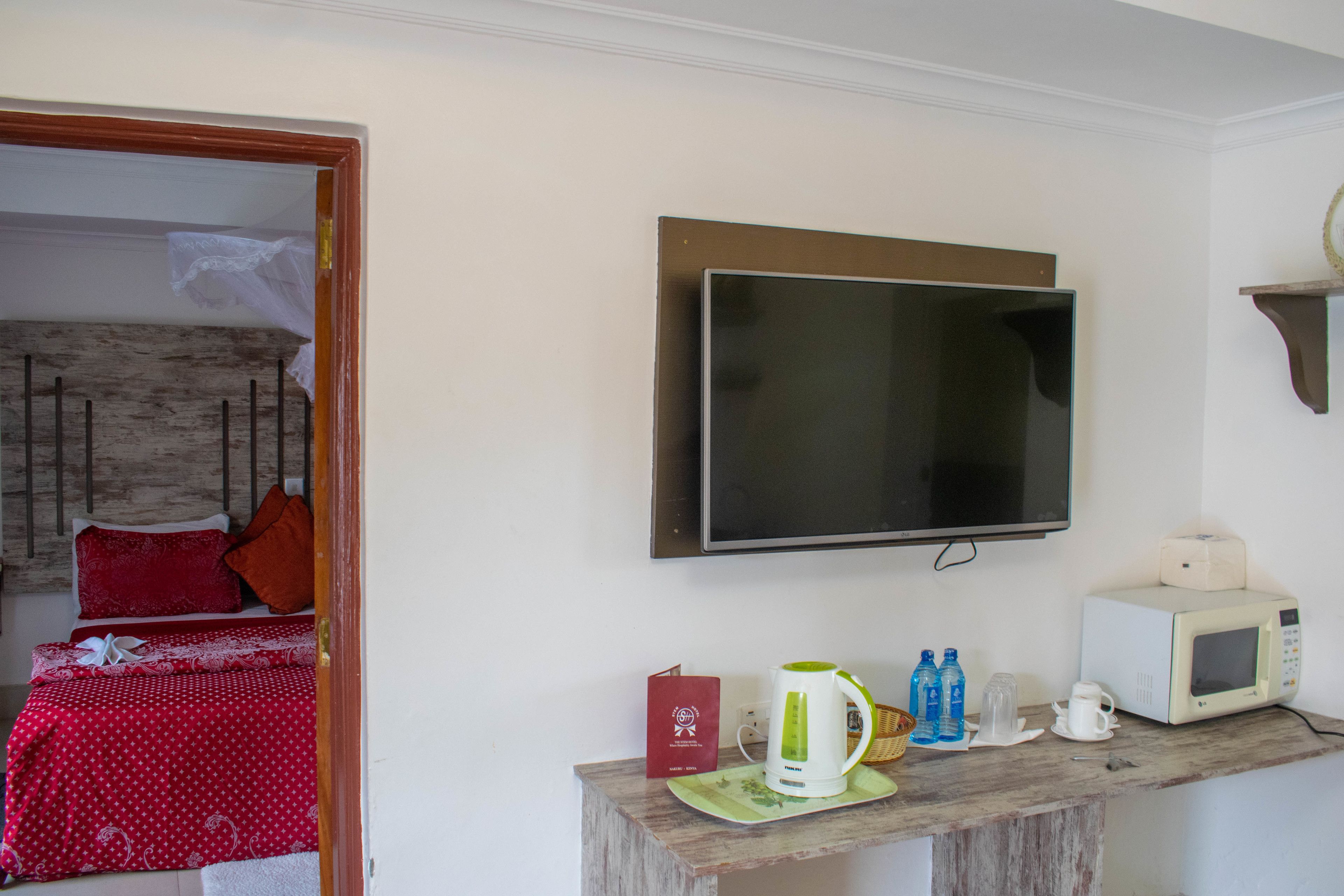 Habitación de hotel con cama, televisión, microondas y una pequeña mesa con tetera y botellas.