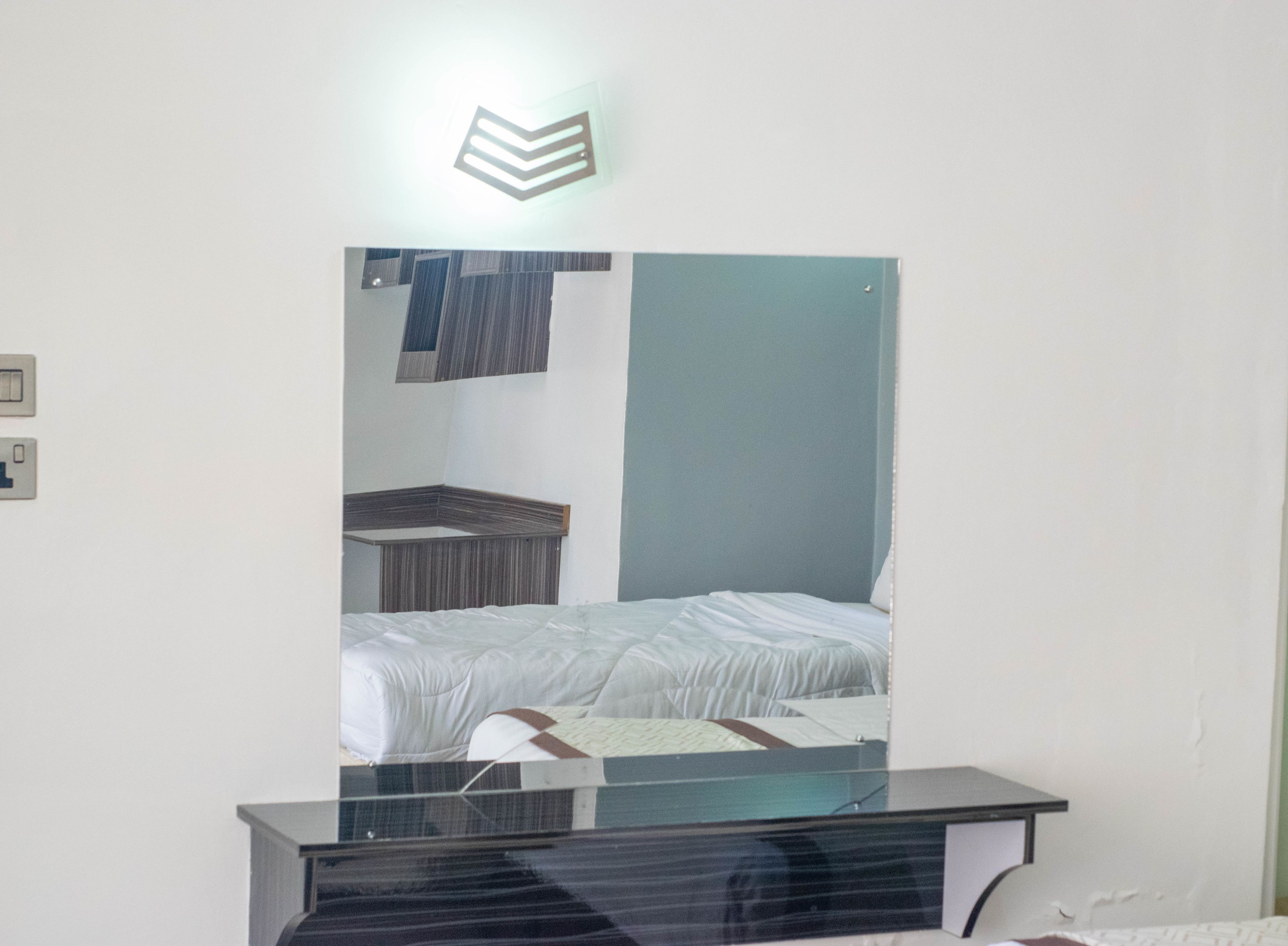 A hotel room with a bed, a mirror, a small table, and a light fixture above the mirror.