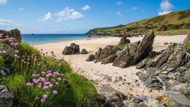 A beach with clear skies, rocky terrain, and green hills in the background. - Port Charlotte Hotel (Islay Island)
