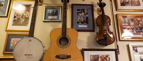 Una habitación con una guitarra, un banjo y un violín colgados en la pared, junto con varias fotografías enmarcadas.