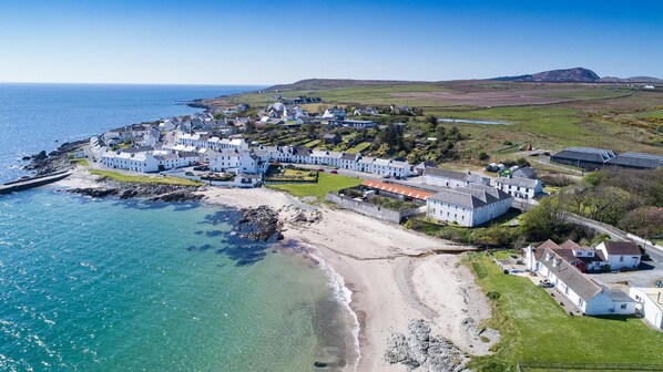 A coastal village with white buildings, a beach, and a rocky shoreline.